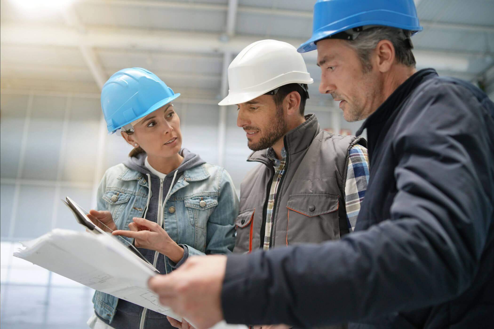 Construction professionals in hard hats reviewing plans and a tablet on site